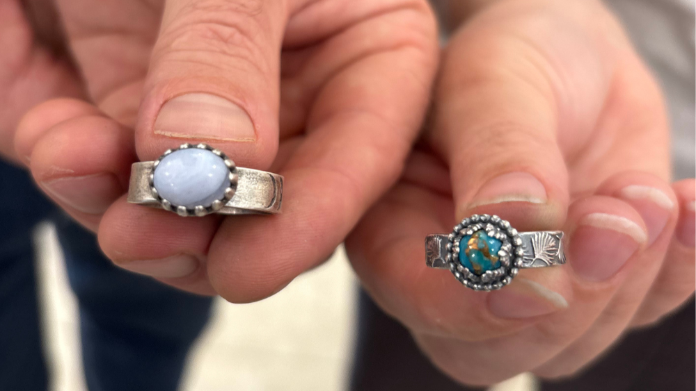 Two silver rings with gemstones held between fingers against a blurred background